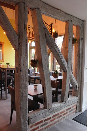 A rustic interior with exposed wooden beams, hanging planters, and a brick wall. - Hôtel de la Bonnheure (Bracieux)