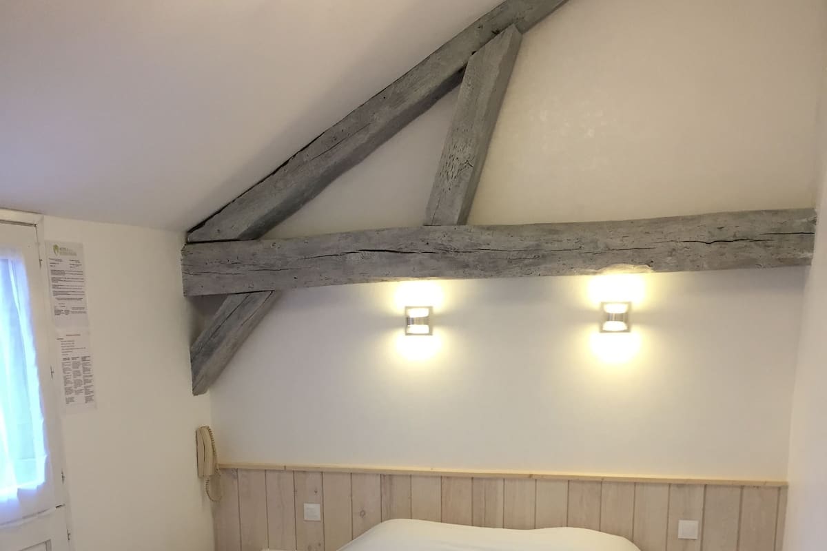 A bedroom with a wooden ceiling, a bed with white bedding, and two bedside lamps.