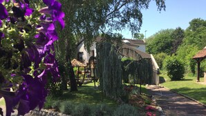 A garden with a pergola, a stone wall, and a pathway leading to a house with a tiled roof.