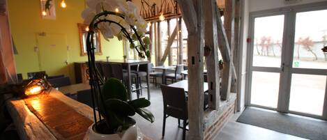 A restaurant interior with wooden tables, chairs, hanging light fixtures, and a potted plant on a wooden bench.