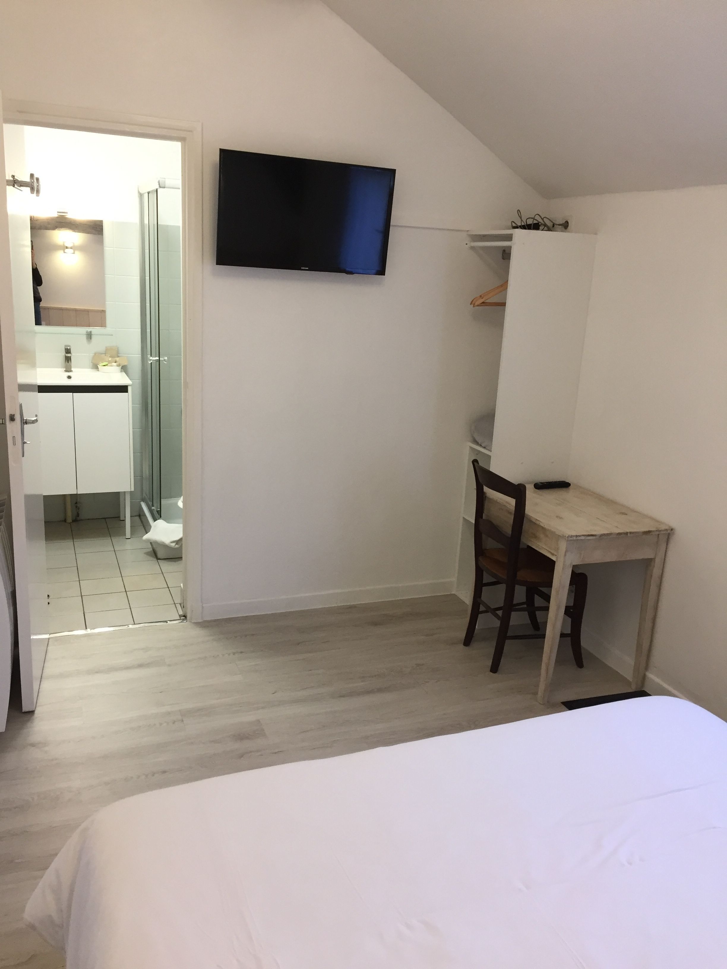 A bedroom with a bed, a desk with a chair, a TV mounted on the wall, and a bathroom with a shower and sink.