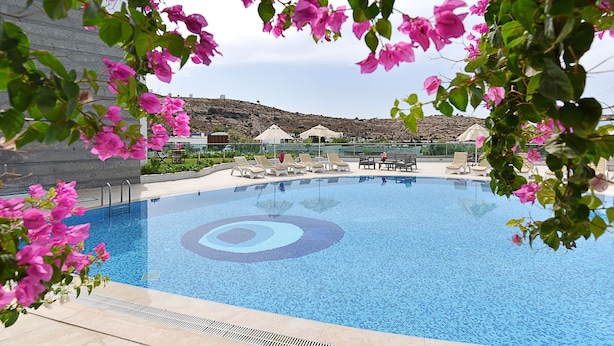 A swimming pool with lounge chairs and umbrellas, surrounded by greenery and hills in the background. - Royal Palm Residence (Bodrum)