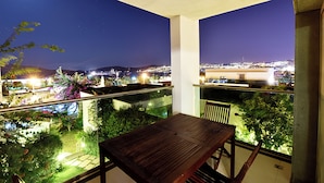 A balcony with a wooden table and chairs, overlooking a cityscape at night. - Royal Palm Residence (Bodrum)