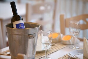A bottle of Paros wine in a metal bucket on a table with two empty wine glasses and a candle.