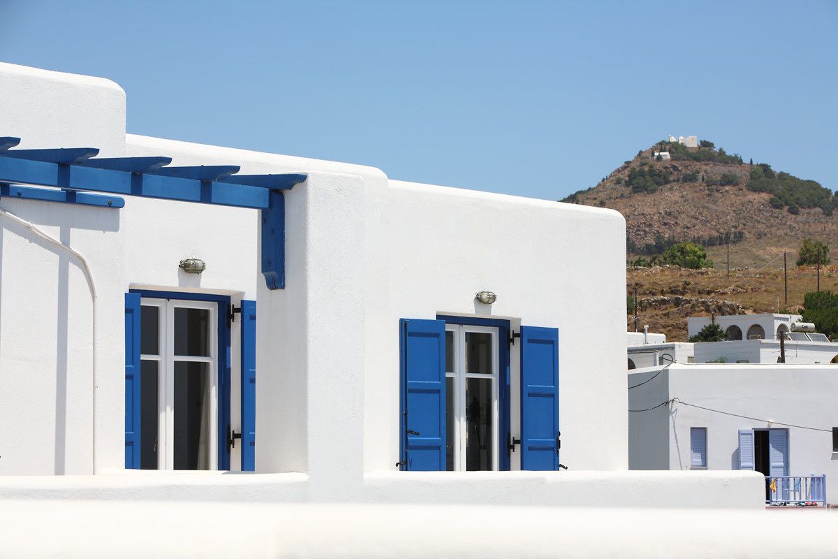 Ein weißes Gebäude mit blauen Fensterläden und freiem Blick auf einen Hügel im Hintergrund.