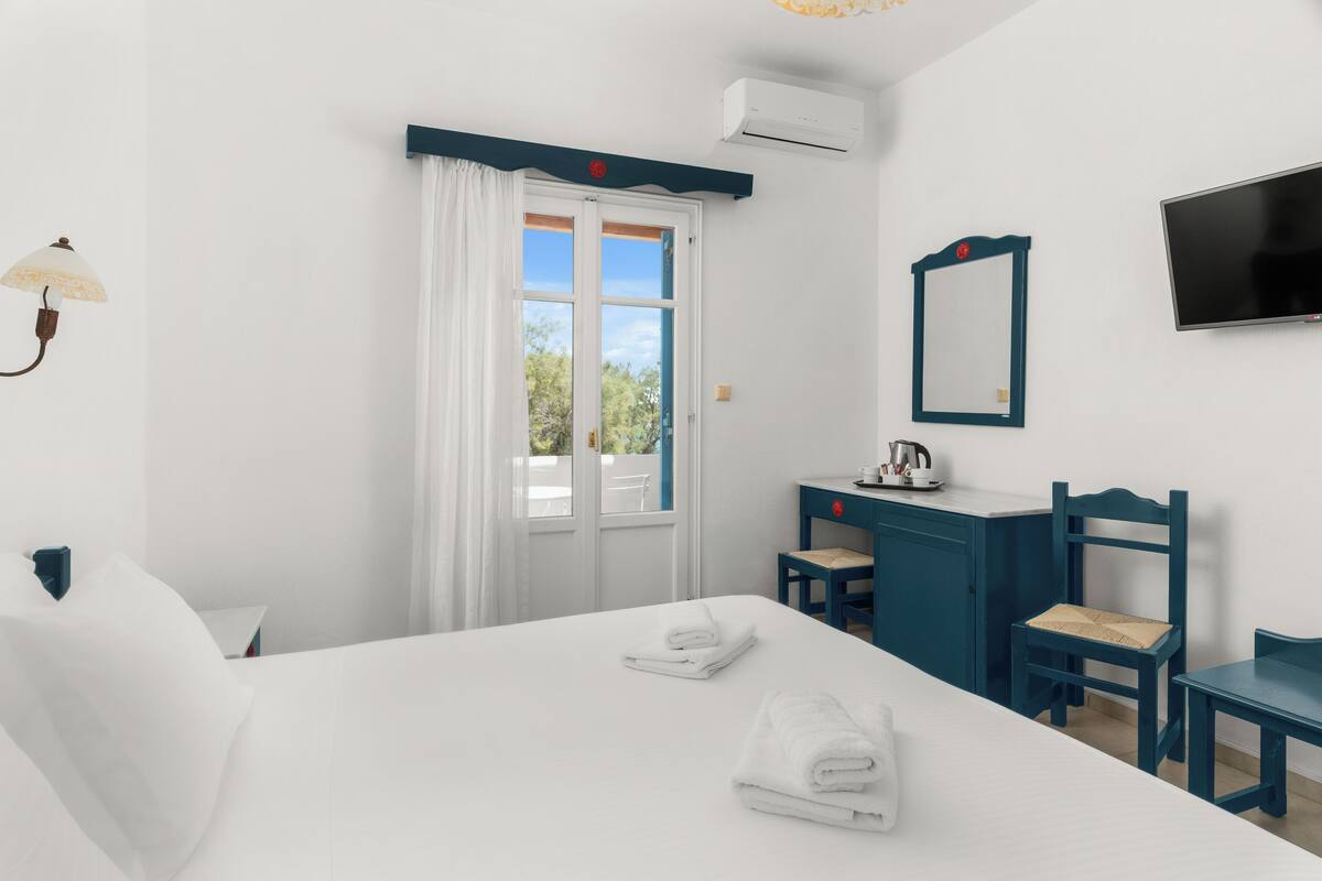 Habitación de hotel con cama, escritorio, silla, televisor y ventana con cortinas.