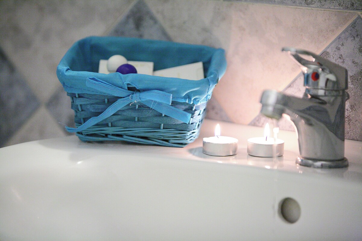 A bathroom sink with a blue basket containing toiletries, two lit candles, and a faucet.