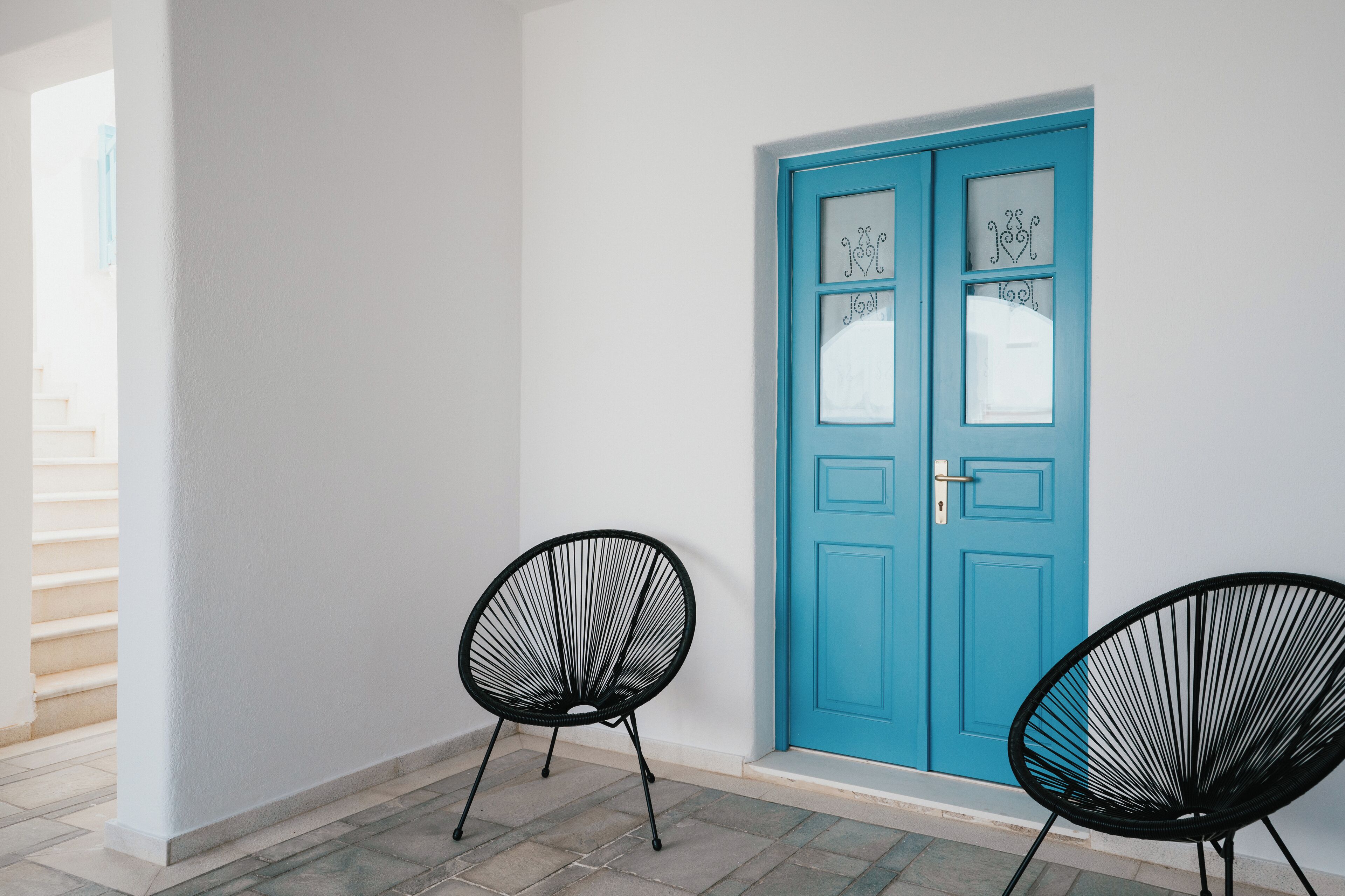 A room with a blue door, two black chairs, and a staircase.