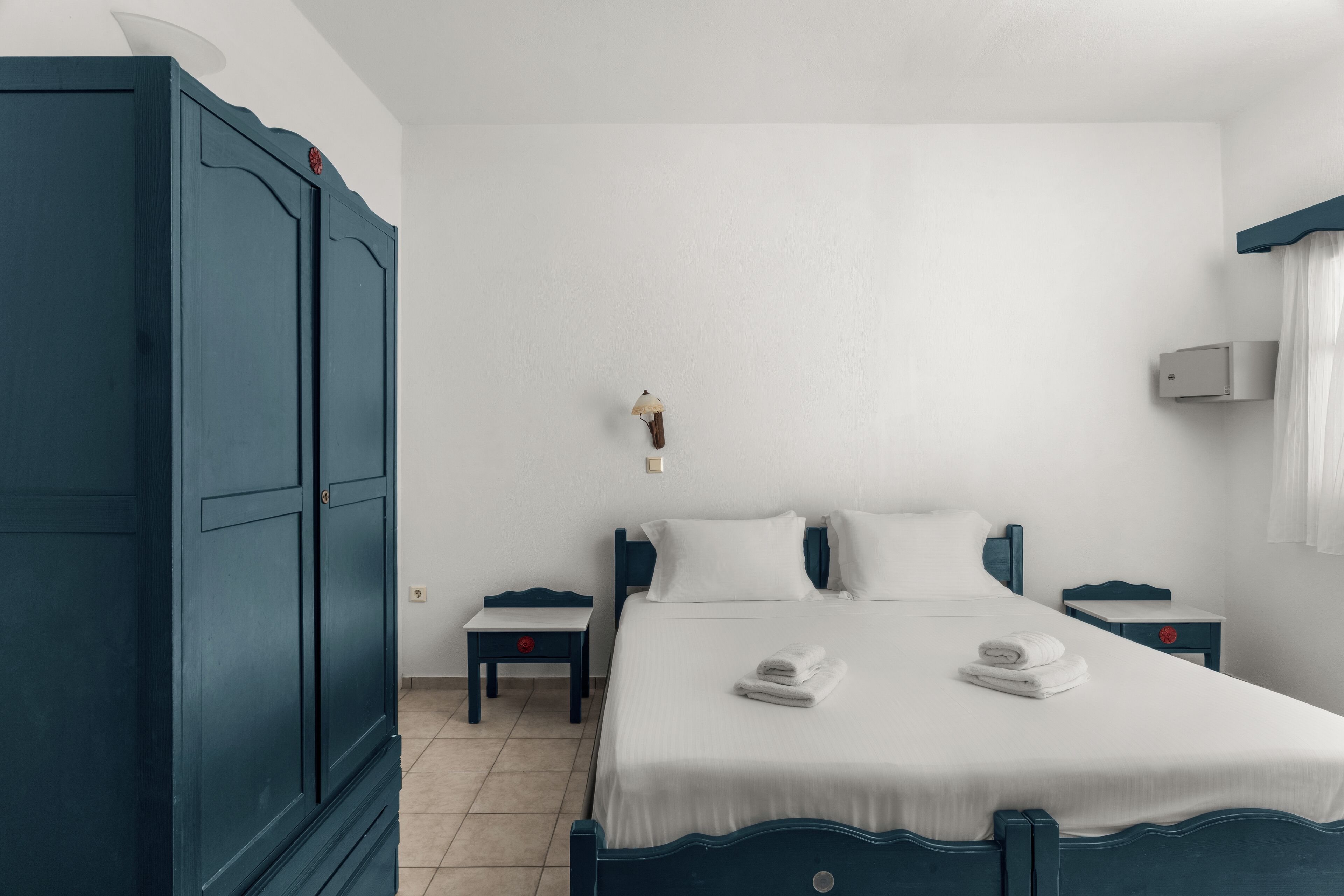 A bedroom with a large bed, two bedside tables, a wardrobe, and a wall-mounted air conditioner.