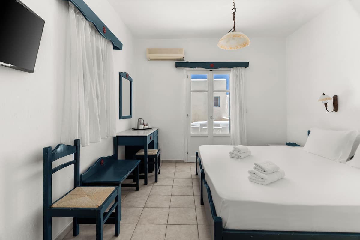 Habitación de hotel con cama, escritorio, silla, televisor y ventana con cortinas.