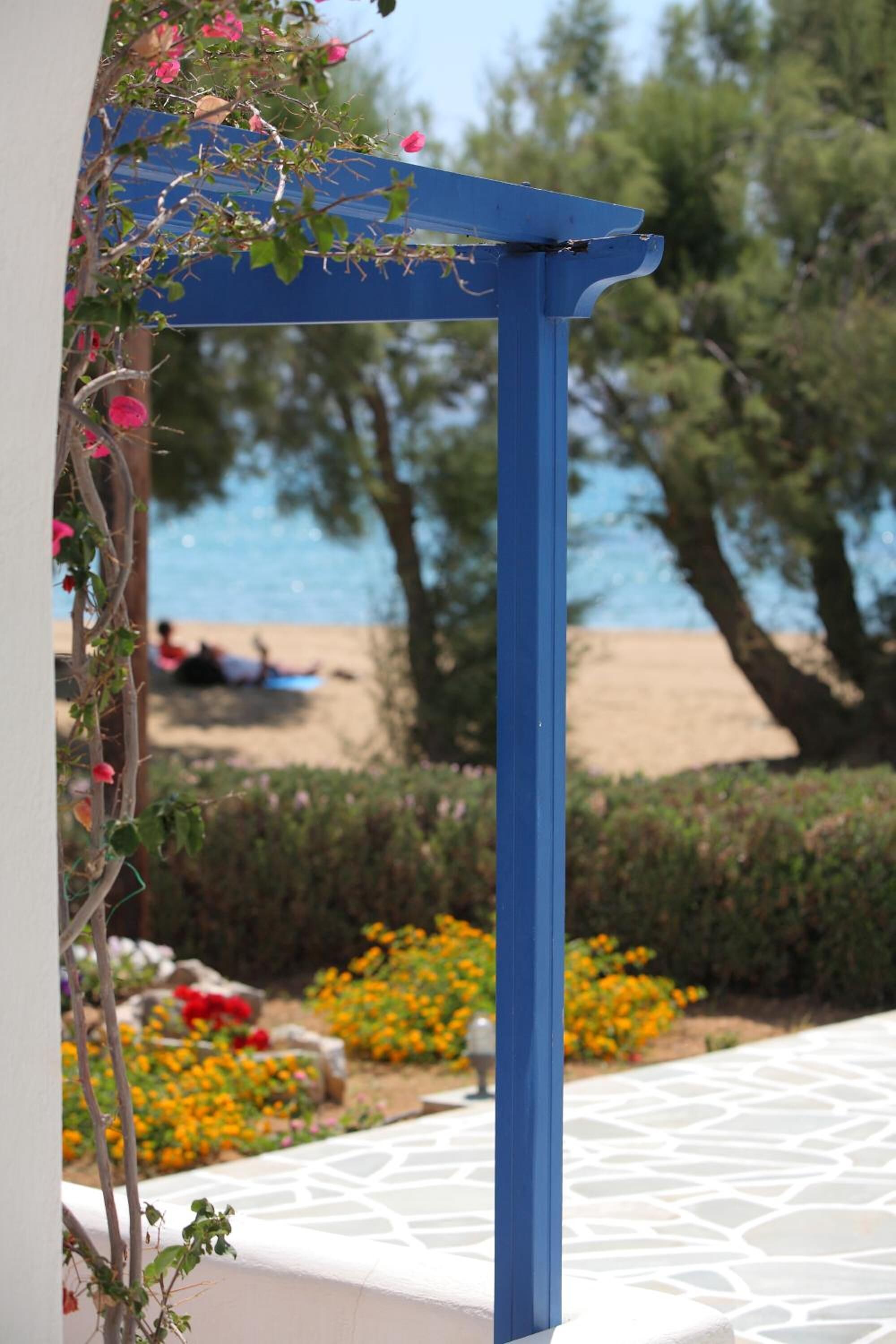 A blue pergola structure with a view of a beach and a person lying on a beach towel.