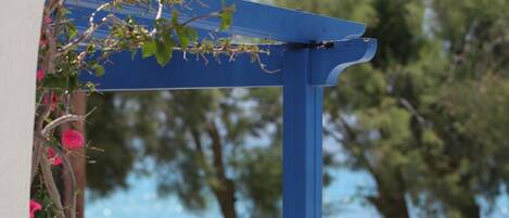 A blue pergola structure with a view of a beach and a person lying on a beach towel.