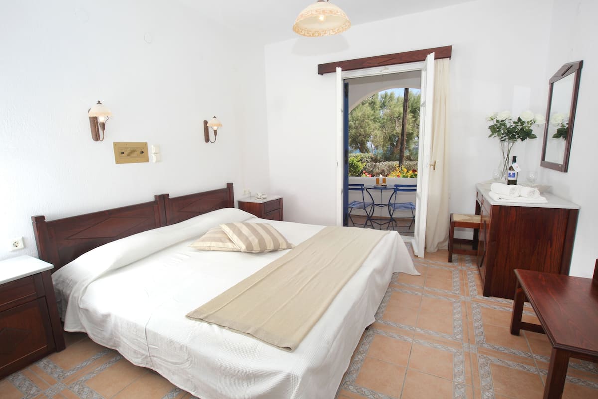 Un dormitorio con cama, mesitas de noche, cómoda, espejo y vistas al exterior.