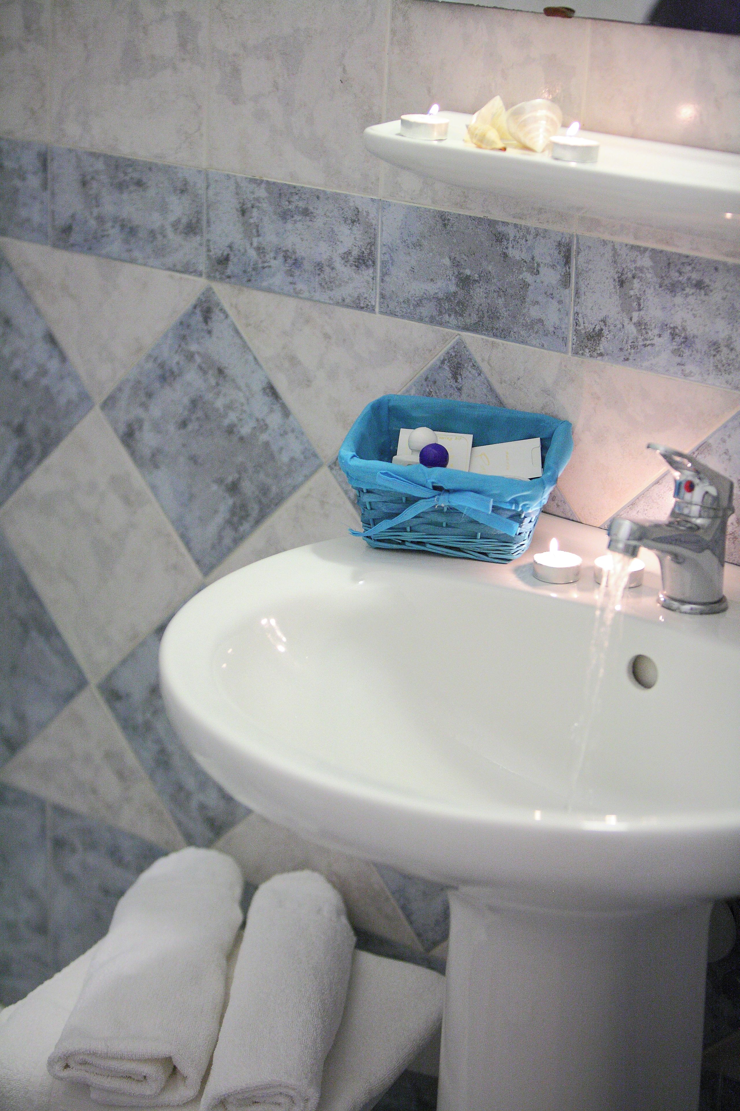 Un baño con un lavabo blanco, una cesta azul y dos velas encendidas.