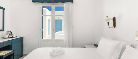 A hotel room with a bed, a desk, a chair, a window with curtains, and an air conditioning unit.