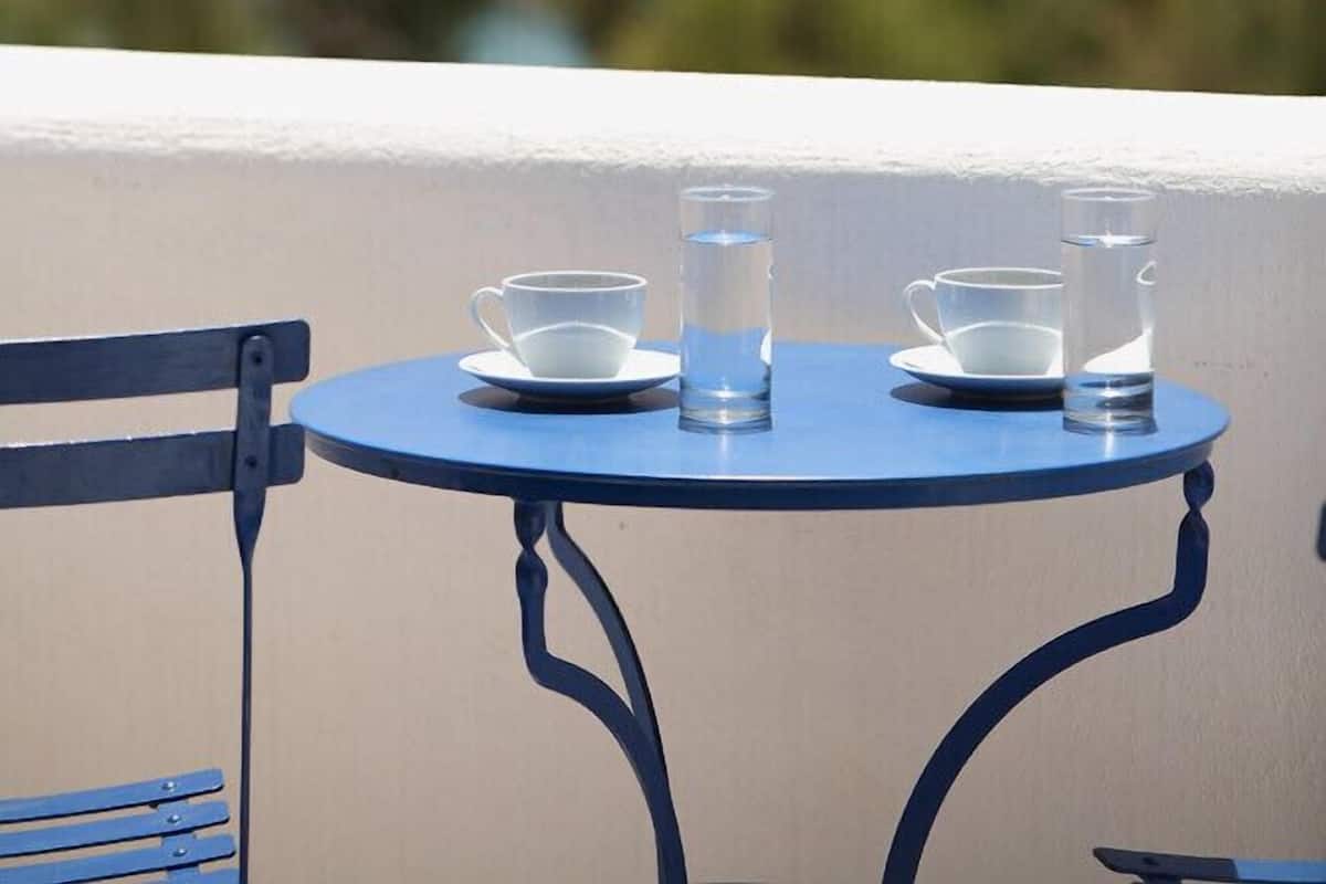 Una mesa redonda con dos tazas blancas y dos vasos transparentes, con el cielo azul y el océano como fondo.