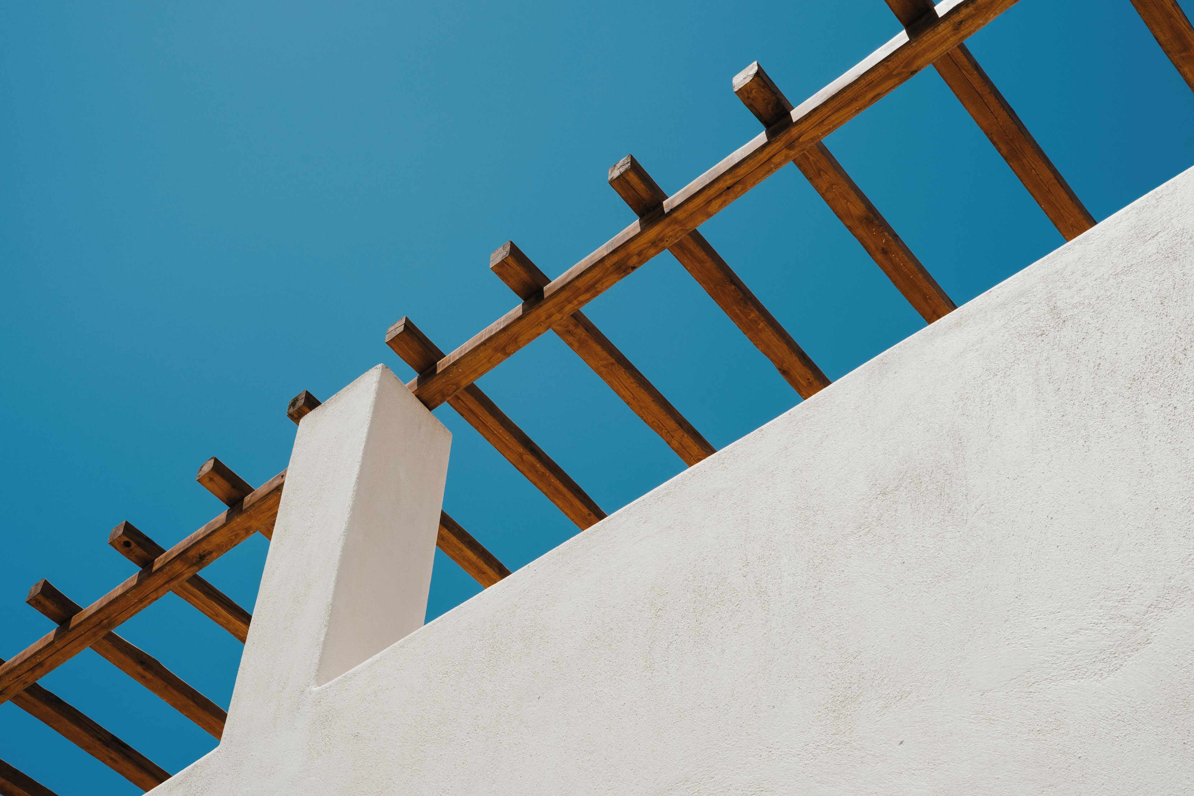 Un mur blanc avec une clôture en bois, sur fond de ciel bleu clair.