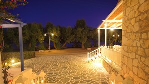 Un espacio al aire libre con suelo de piedra, una pérgola de madera y faroles, que conduce a un edificio con fachada de piedra.