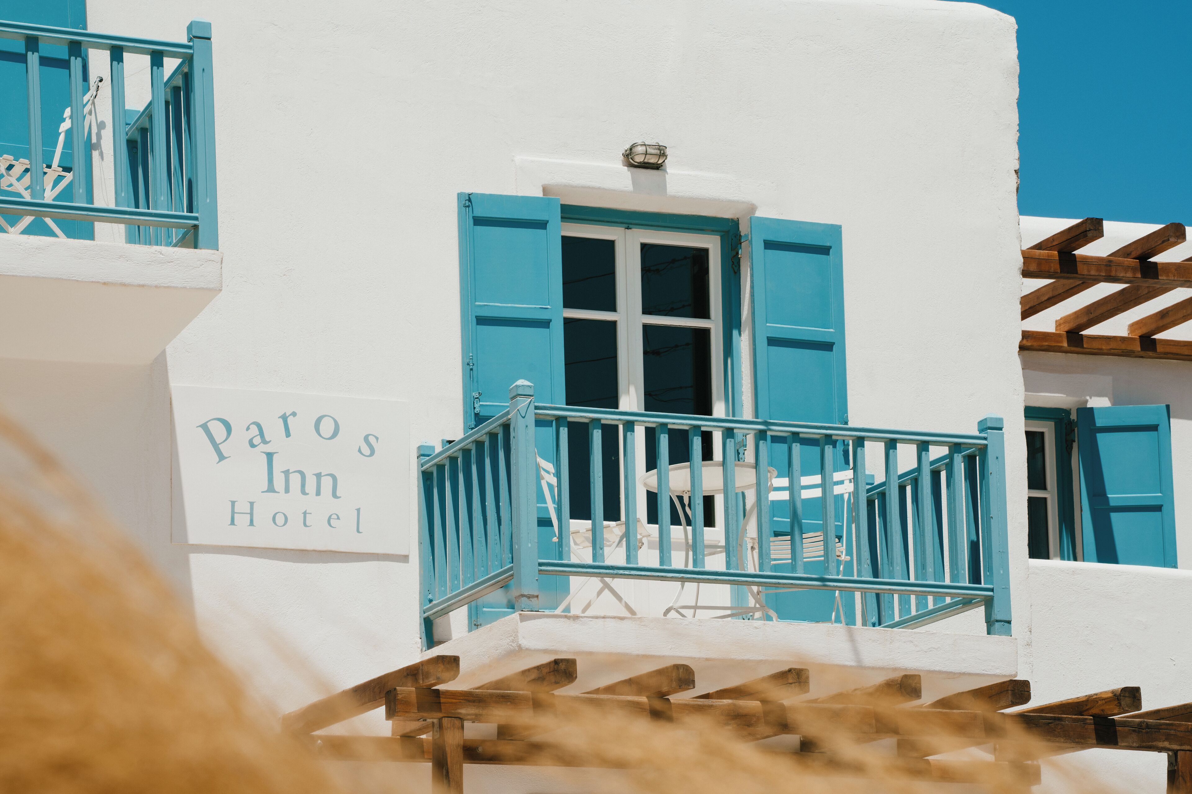 A hotel with a white facade, blue shutters, and a sign reading "Paros Inn Hotel".