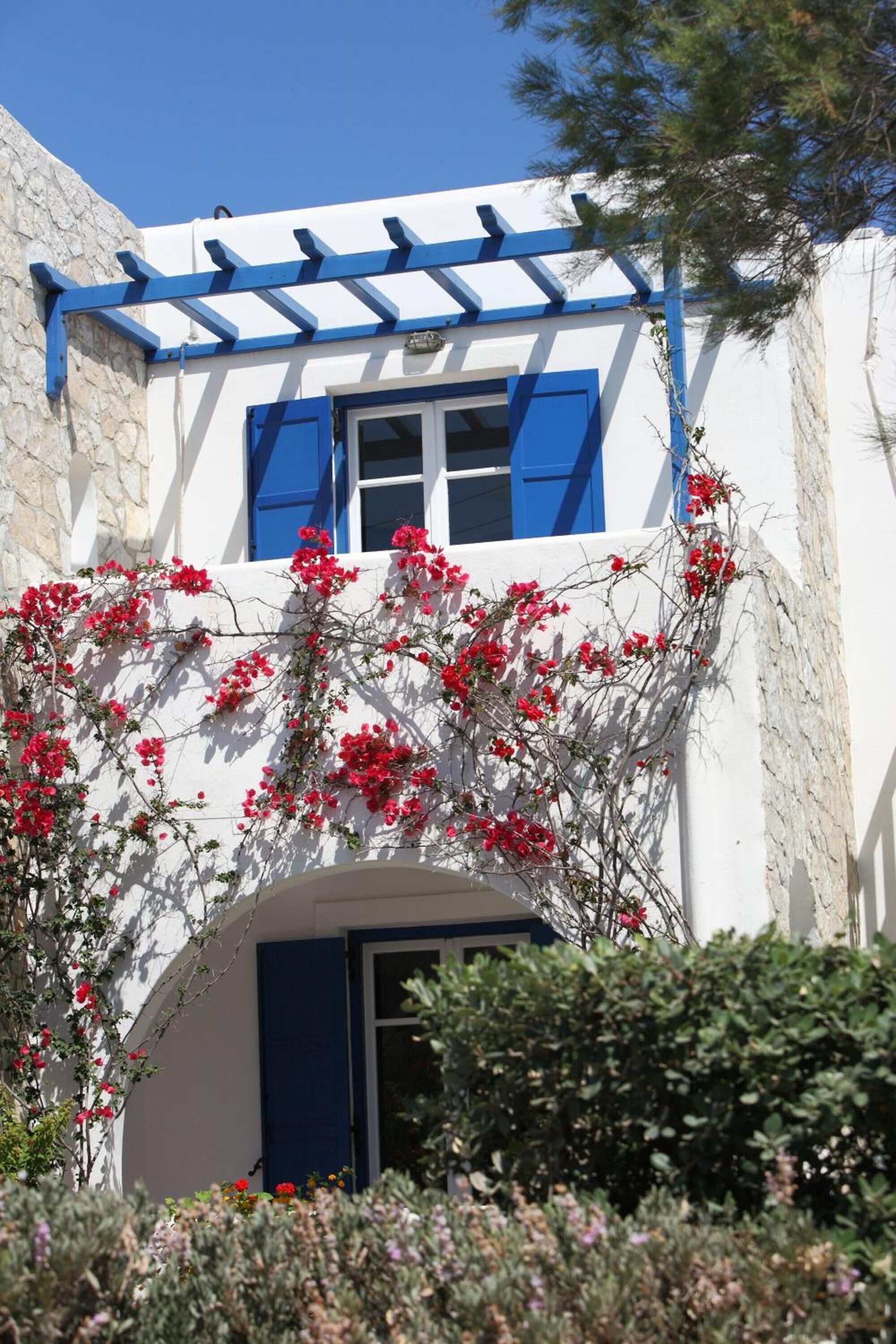 A building with a white facade, blue shutters, and a blue pergola.