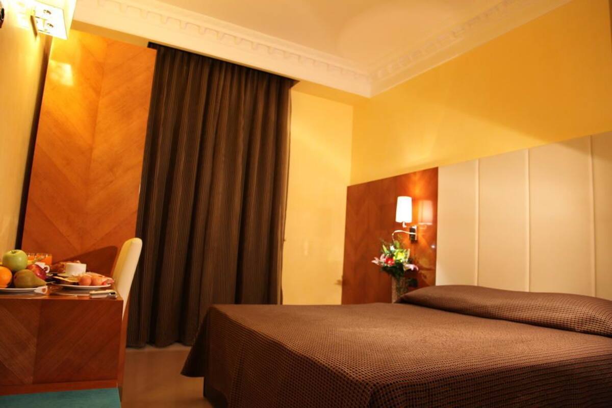 Habitación de hotel con cama, escritorio con lámpara y vista al exterior.