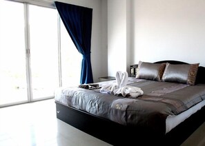 A modern bedroom with a large bed, a nightstand, and a window with blue curtains. - Happy Fish Guesthouse (Patong)