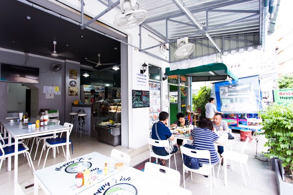 An indoor dining area with tables and chairs, a chalkboard menu, and a counter with food items. - Happy Fish Guesthouse (Patong)