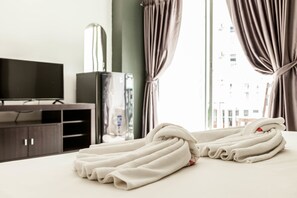 A neatly made bed with folded white towels, a television, and a cabinet in a hotel room. - Happy Fish Guesthouse (Patong)
