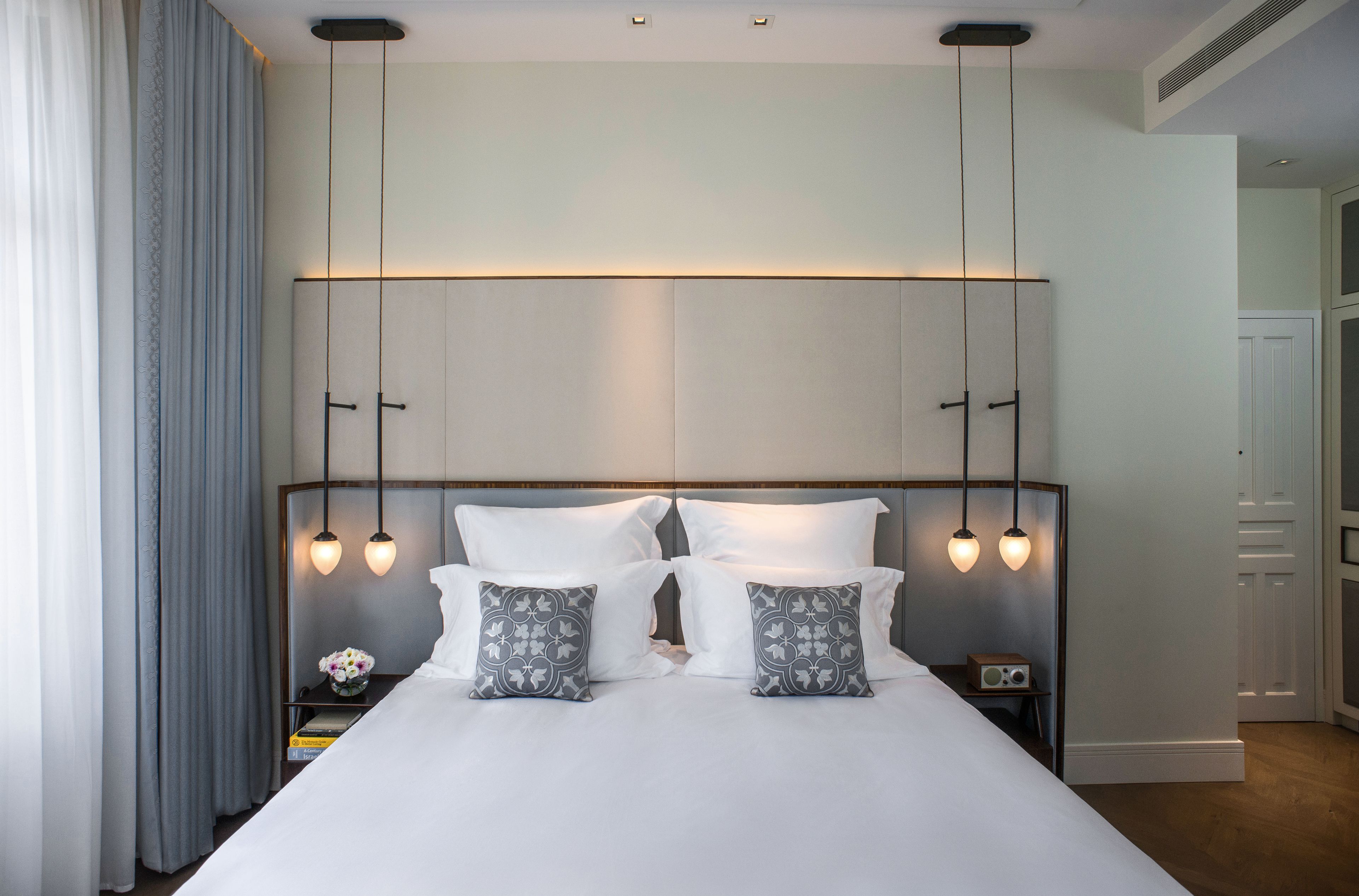 A neatly made bed with two pillows, a bedside table with a radio, and a wall-mounted light fixture.