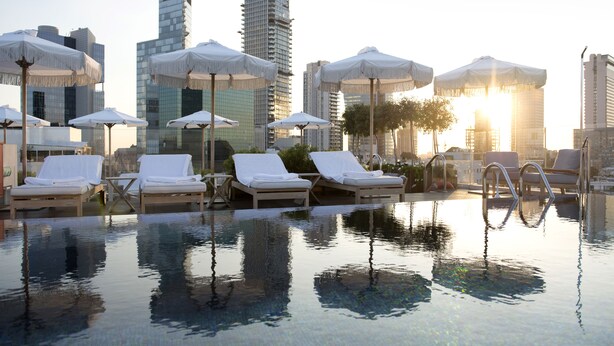 An infinity pool with lounge chairs and umbrellas, surrounded by tall buildings. - The Norman Tel Aviv (Tel Aviv)