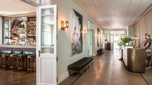 A bar area with stools, a bartender, and a bar counter. There is a reception desk with a receptionist and a phone. The floor is wooden, and there are large windows allowing natural light. - The Norman Tel Aviv (Tel Aviv)