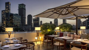 An outdoor dining area with tables and chairs, umbrellas, and a city skyline view in the background. - The Norman Tel Aviv (Tel Aviv)
