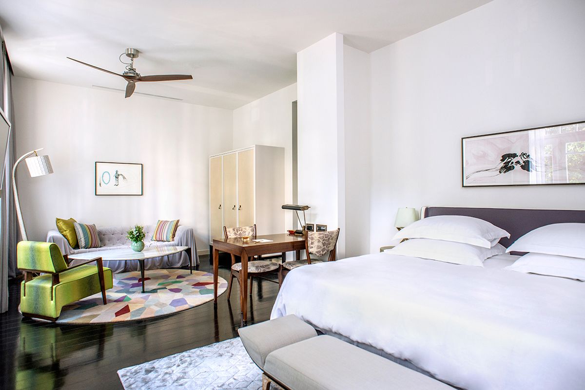 A modern hotel room with a bed, a desk, a chair, a sofa, and a ceiling fan.