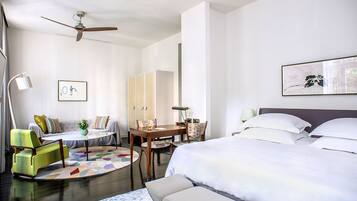 A modern hotel room with a bed, a desk, a chair, a sofa, and a ceiling fan.