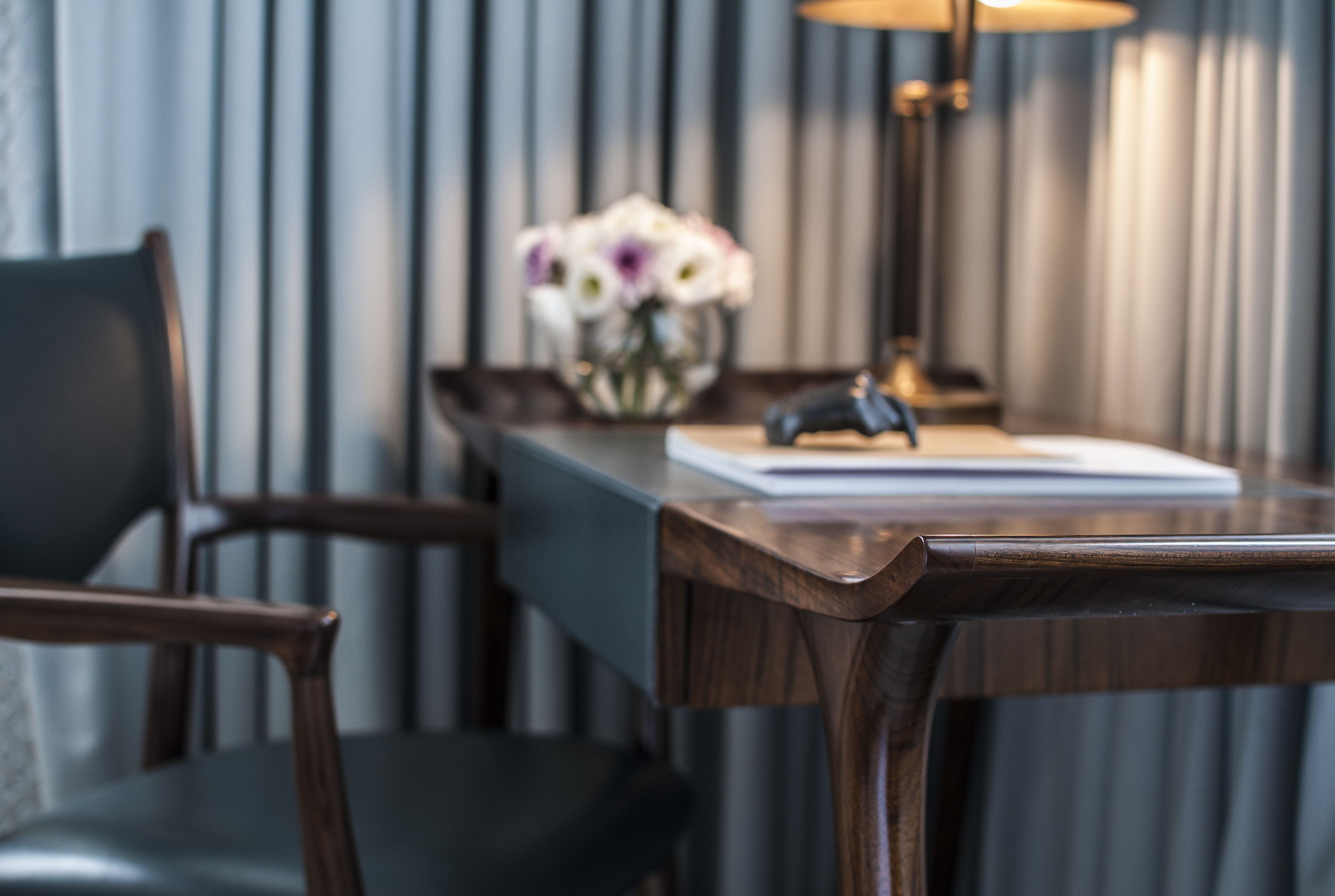Un bureau en bois, orné d’un vase de fleurs, d’une lampe et d’un livre.