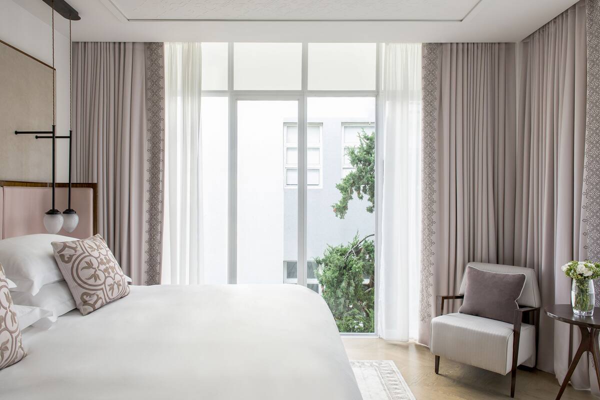 A modern hotel room with a large bed, a sitting area, and a view of the outdoors.