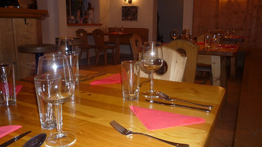 Una mesa de comedor dispuesta con copas de vino, cubiertos y servilletas rosas.