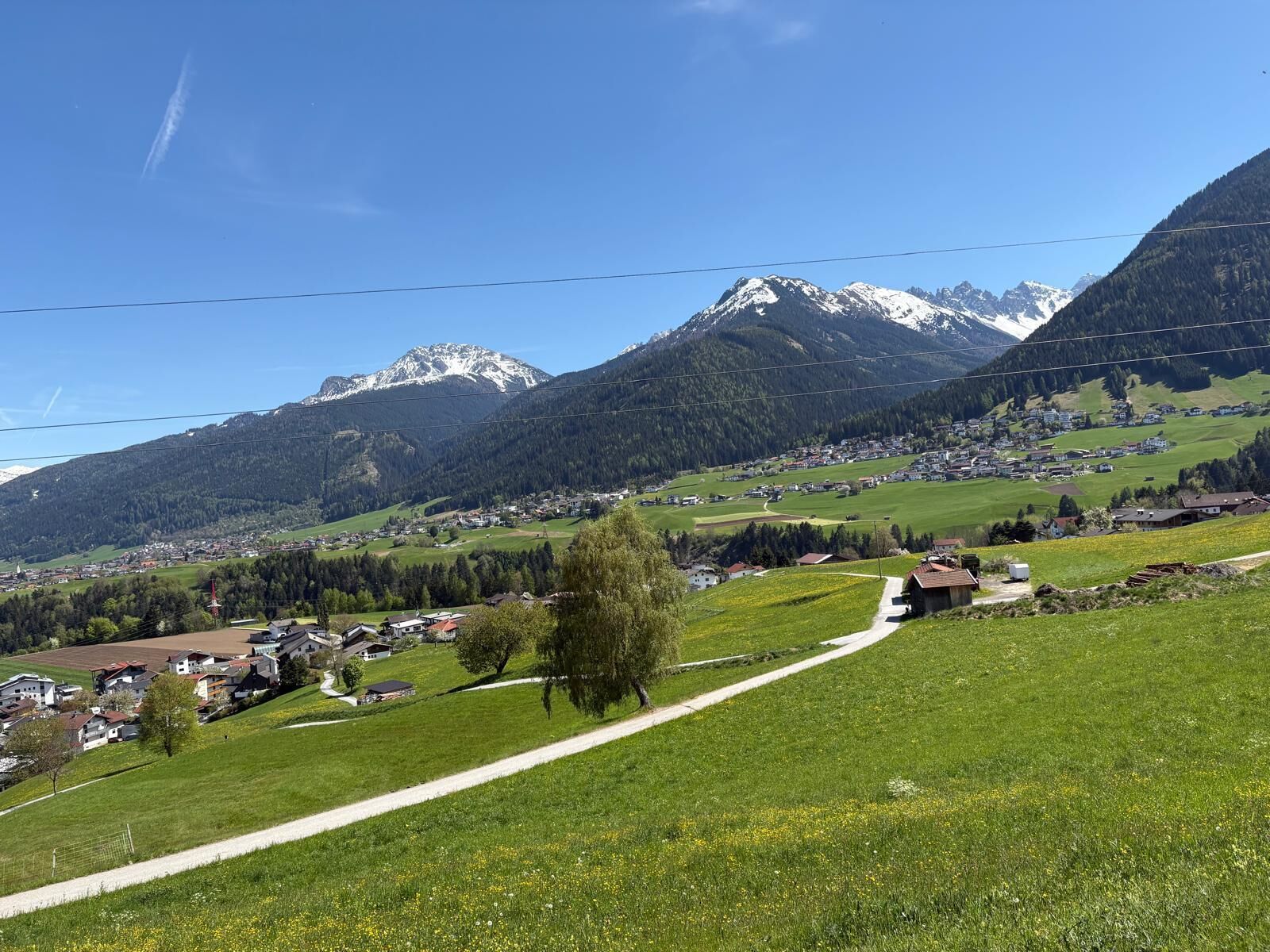 Paisaje rural con cielo despejado, un camino sinuoso y un pueblo con casas, con una montaña al fondo.