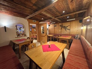 A rustic interior with wooden tables and benches, a wooden ceiling, and a wall-mounted clock.