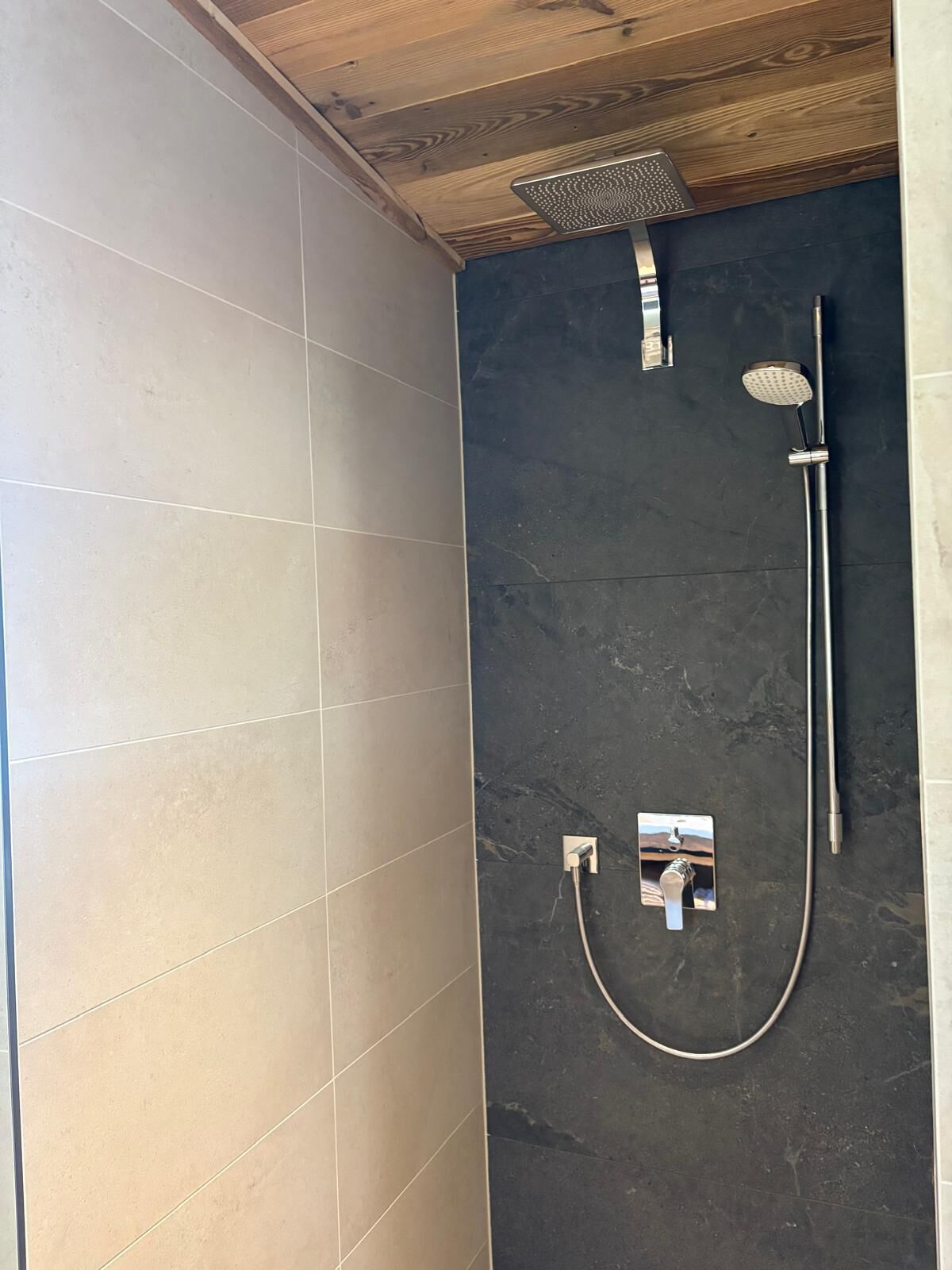 A shower with a rain showerhead, handheld showerhead, and a wall-mounted control panel.