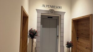 A hallway with a grey elevator, a sign reading 'ALPENRESORT', and two potted plants. - Alpenresort Panorama (Oberperfuss)