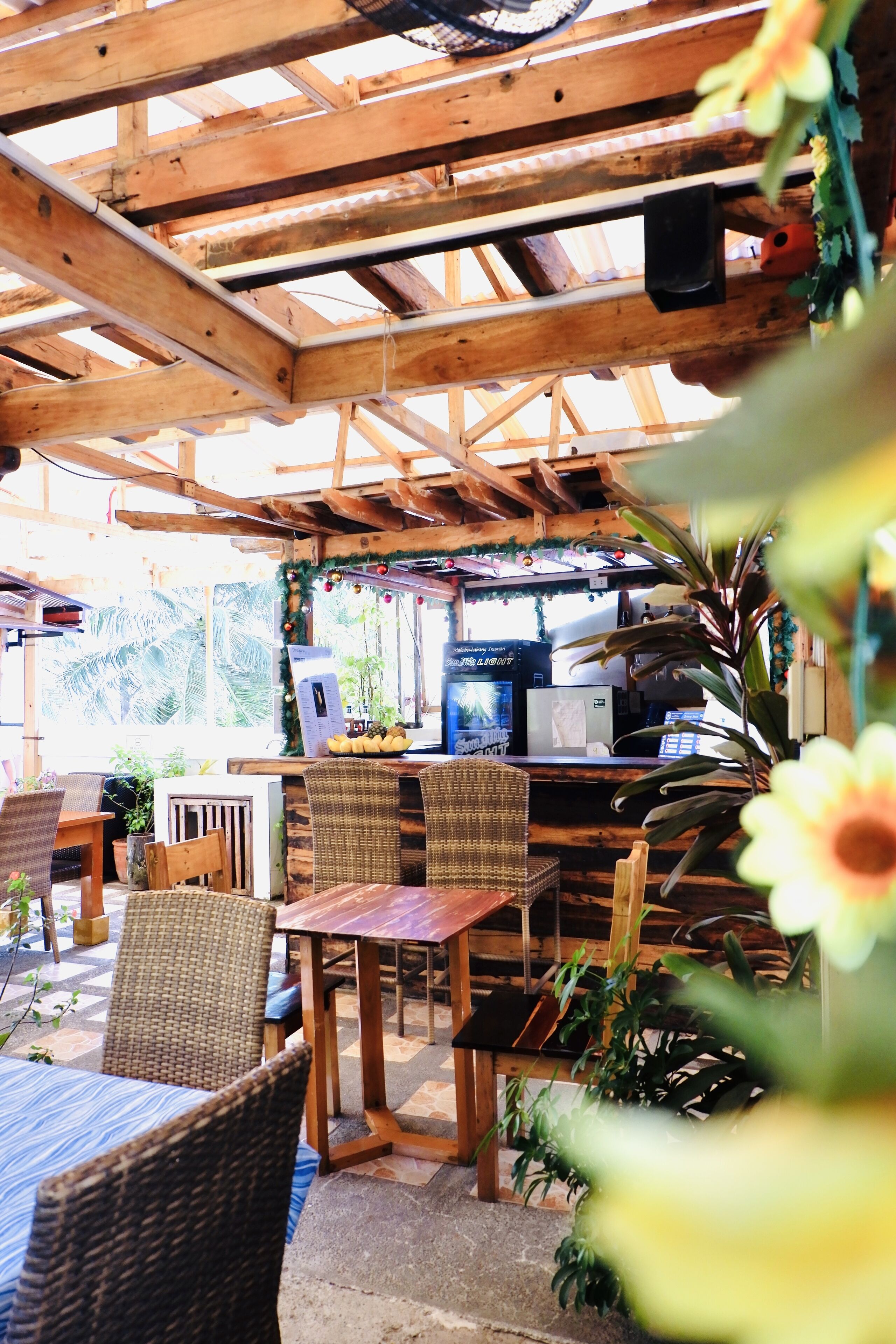 A wooden pergola structure with tables and chairs, a coffee machine, and potted plants.