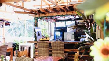 A wooden pergola structure with tables and chairs, a coffee machine, and potted plants.
