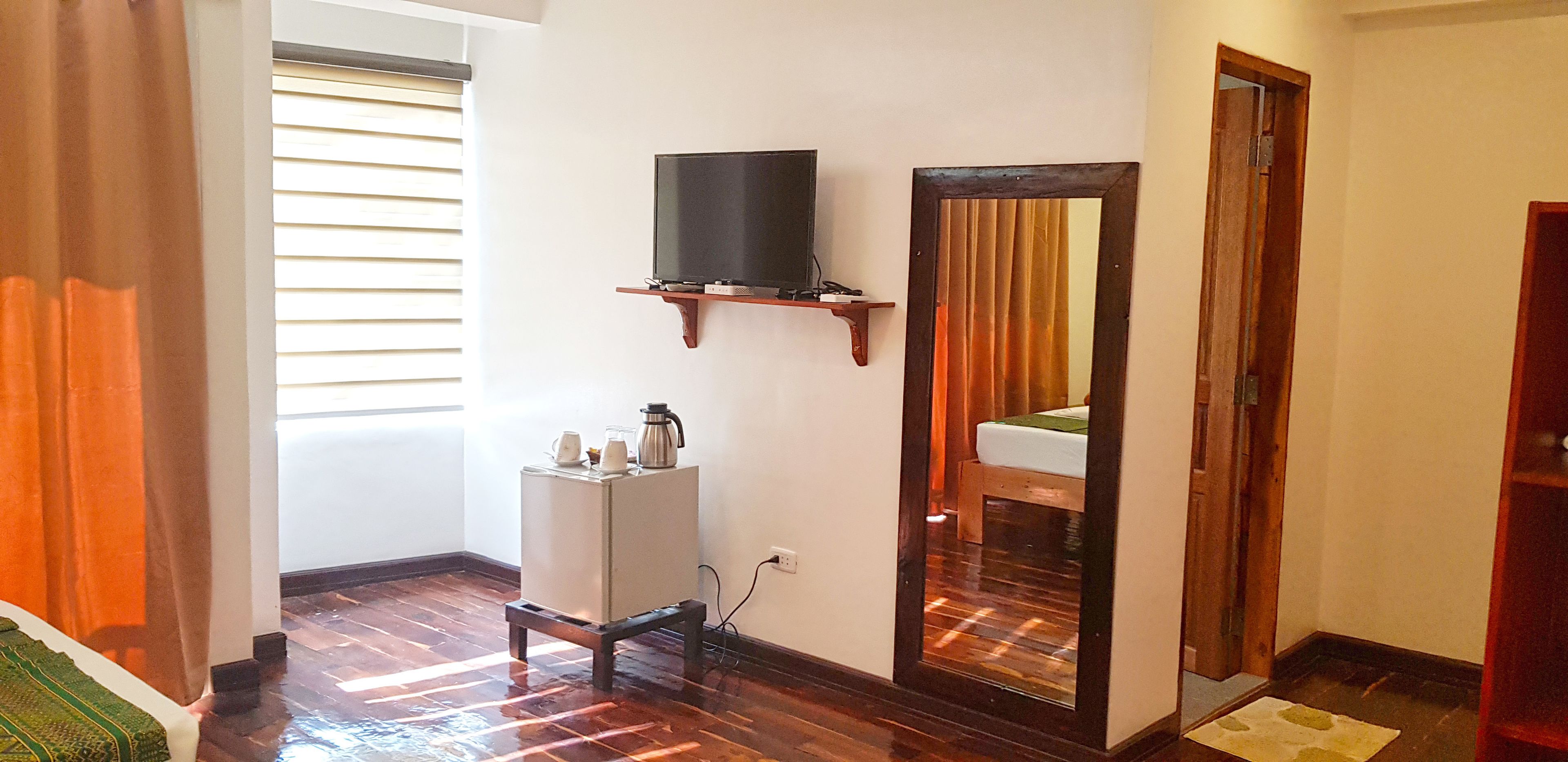 A room with a wooden floor, a small white cabinet, a television on a wooden shelf, and a mirror on the wall.