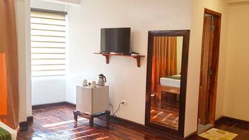 A room with a wooden floor, a small white cabinet, a television on a wooden shelf, and a mirror on the wall.