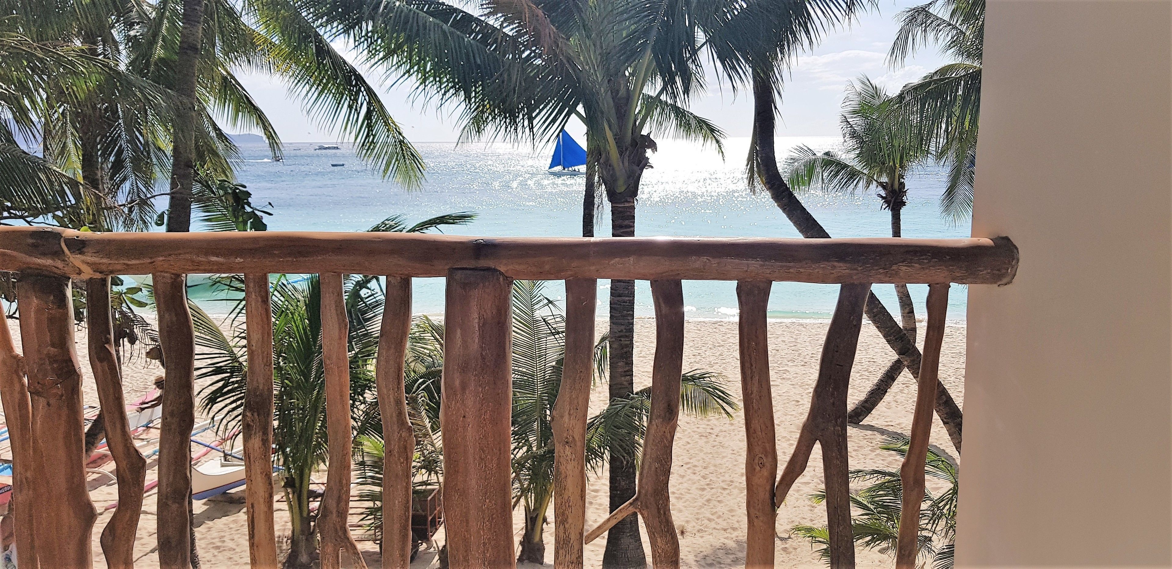 Barandilla de madera con vista a una playa, palmeras y una vista despejada del océano.