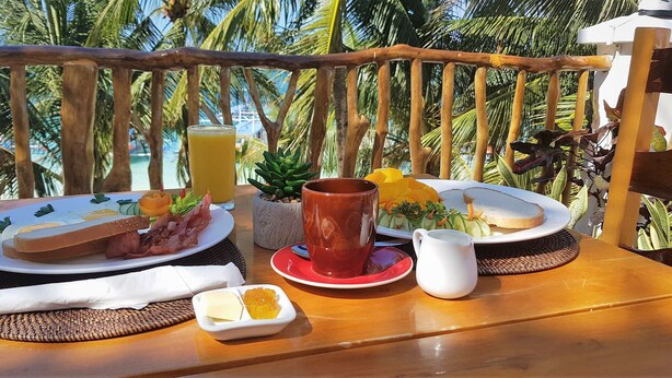 A breakfast setup on a wooden table with plates of food, a pitcher, and a cup, overlooking a beach with palm trees. - DiveGurus Boracay Beach Resort (Boracay Island)