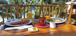 A breakfast setup on a wooden table with plates of food, a pitcher, and a cup, overlooking a beach with palm trees. - DiveGurus Boracay Beach Resort (Boracay Island)