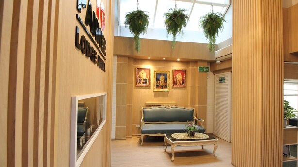 Un hall d’entrée avec un comptoir de réception en bois, un canapé, une table basse et des plantes suspendues.
