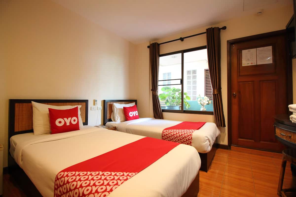 Een hotelkamer met twee bedden, elk met een rood-witte dekbedovertrek, en een raam met gordijnen.